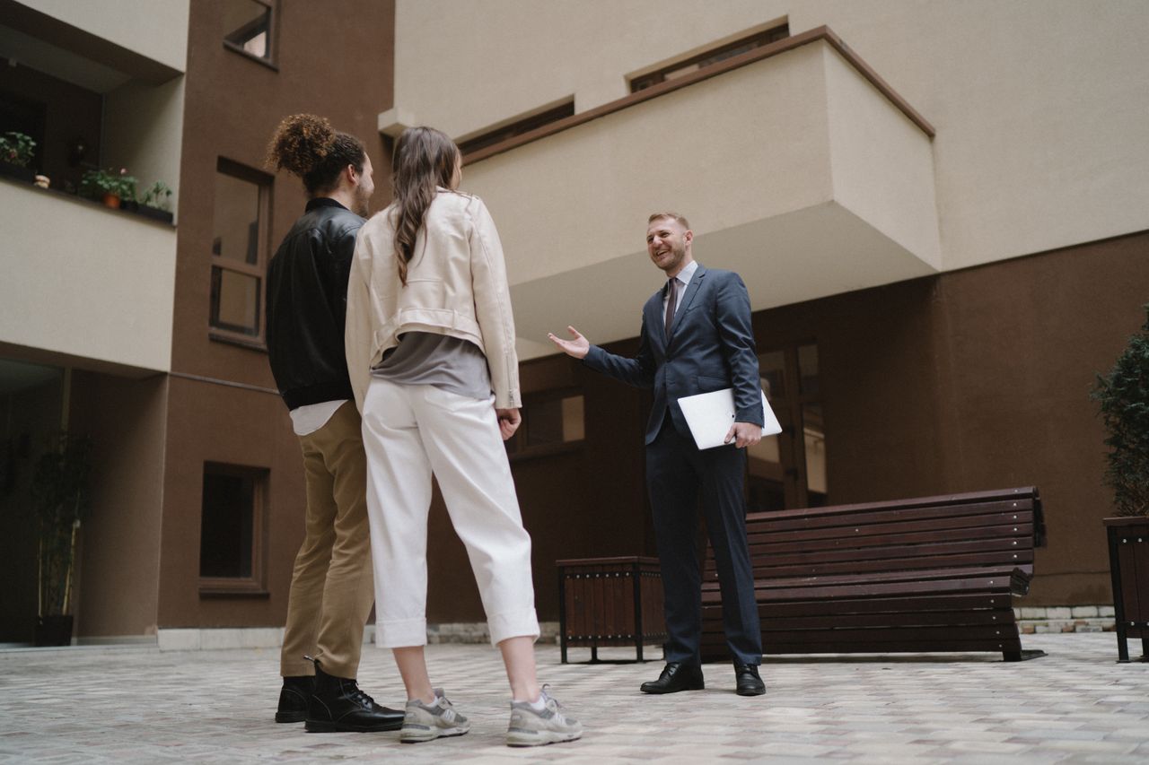 A realtor converses with a couple in a modern apartment courtyard.